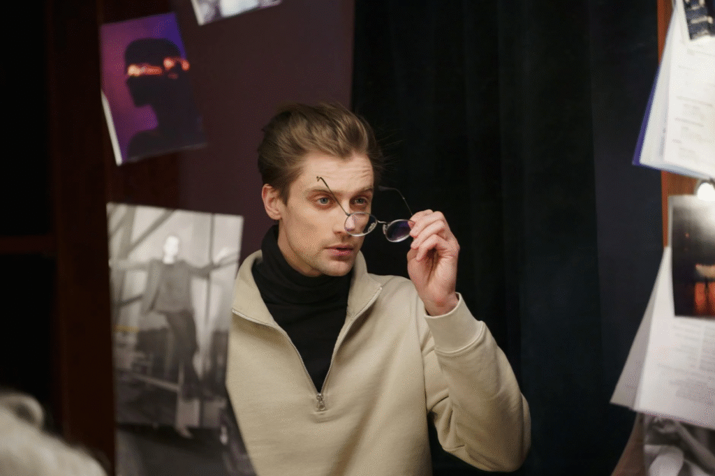 Actor preparing for a role backstage in a dressing room, adjusting glasses and looking at the mirror.