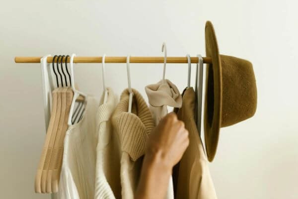 Stylish beige and brown clothes on a rack with a hand reaching in.